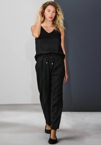 Top negru fără mâneci cu decolteu în V, asortat cu pantaloni negri largi cu talie ajustabilă prin șnur și accente decorative argintii. Pantofi negri comozi.