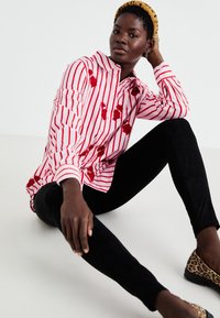 Chemise rayée rouge et blanche avec broderies florales, associée à un legging noir et des ballerines à imprimé léopard. Un bandeau jaune texturé complète le look.