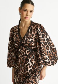 Leopard print dress in silk-like fabric, featuring puff sleeves, a deep V-neckline, and delicate black lace accents. Brown and cream tones.
