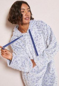 Fleece kapucnis pulóver világoskék színben, leopárdmintával. Húzózsinóros kapucni, nagy elülső zseb és széles ujjak jellemzik. Puha tapintású.