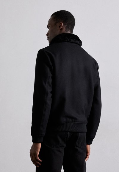 Svart sweatshirt med en faux fur-krage, ribbade ärmslut och nederkant, som har en slät yta och en figurnära design. Bakvyn visar rena linjer.