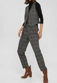 Grijs geruit pak met een getailleerd vest met een ingesneden kraag en vijf knopen, gecombineerd met taps toelopende broeken en bruine enkellaarsjes met hak.