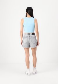 Světle modrý bezrukávový crop top, šedé džínové šortky s vysokým pasem a bílé tenisky s černými detaily, pohled zezadu.