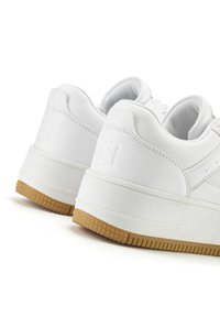 White leather sneakers with a textured surface, padded collar, and a gum rubber outsole featuring small star patterns.