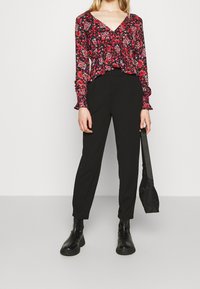 Blumenmuster Langarm-Crop-Top in Schwarz, Rot und Weiß mit geschmückten Details; kombiniert mit hochgeschnittenen schwarzen Hosen und schwarzen Stiefeletten.