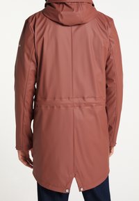 Vattentålig brun kappa med huva, med en slät textur, dragsnöre i midjan och tryckknappar vid fållen.