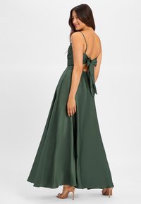 Groene satijnen maxi-jurk met een aansluitende top, dunne bandjes, een open rug en een grote strikaccent bij de taille, die overloopt in een volle rok.