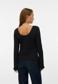 Czarny top z długim rękawem o teksturowej powierzchni, z niskim dekoltem na plecach i dopasowanym kroju. Połączony z ciemnoniebieskimi dżinsami o wysokim stanie.