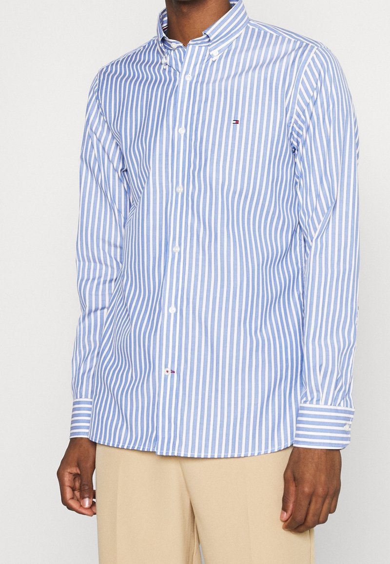 Overhemd met knopen, gemaakt van licht katoen, met blauw-witte verticale strepen, lange mouwen en een klein logo op de borst.