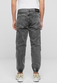 Pantalones jogger de mezclilla negra con puños elásticos, cinco bolsillos y costuras decorativas. Presenta una etiqueta en la parte trasera de la cinturilla.