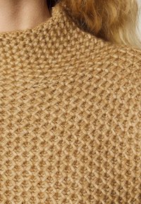 Maglione lavorato a maglia con un motivo testurizzato in beige caldo, con colletto alto e un aspetto intrecciato, che mette in mostra un filato morbido e spesso.