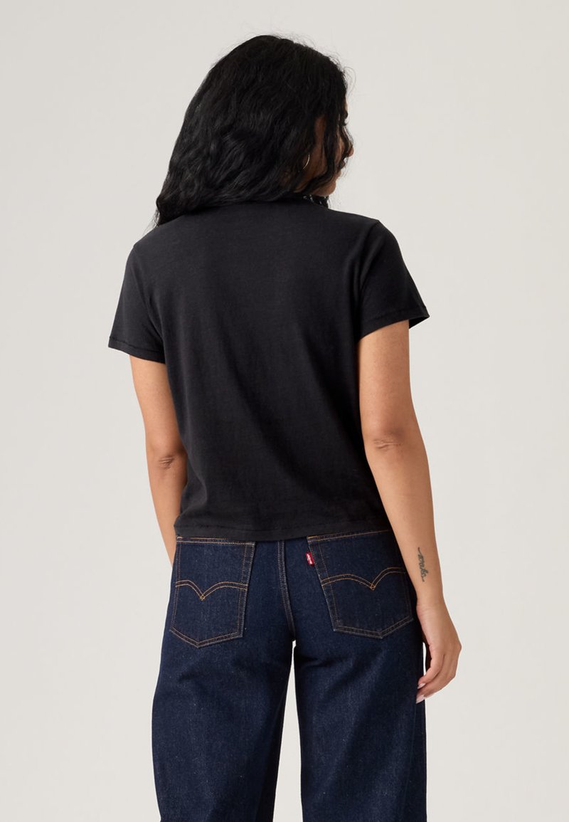 T-shirt noir à manches courtes avec une coupe décontractée, associé à un jean en denim foncé avec des coutures contrastées et des détails sur la poche arrière.
