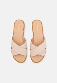Sandales à glissière à brides croisées beiges avec une tige synthétique lisse, une semelle intérieure rembourrée et des coutures décoratives le long des bords de la semelle.