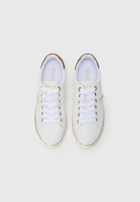 Hvite sneakers med en glatt lærfinish, gullfargede detaljer og snøring. Teksturert beige hældetalj. Logo synlig på tungen.