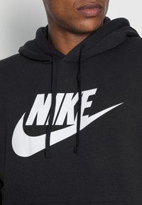 Sudadera negra de algodón con capucha ajustable. Presenta un destacado logo blanco de "NIKE" y un diseño de swoosh en el pecho.