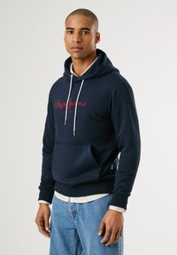 Marineblauwe hoodie met trekkoord, voorzak, ribgebreide manchetten en zoom. Heeft een "Pepe Jeans London" logo in bordeauxrood. Zachte stoftextuur.