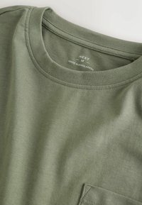 Olivegrünes Baumwoll-T-Shirt mit Rundhalsausschnitt, ausgestattet mit einer kleinen Brusttasche und doppelt genähten Säumedetails. Das Etikett trägt die Aufschrift "NEXT, M."