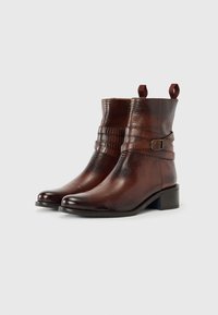 Bottines en cuir marron avec une finition texturée, dotées d'une sangle à boucle et de tirettes, reposant sur un petit talon carré.