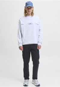 Jasnoszara bluza z nadrukiem, ciemne spodnie cargo i srebrne buty sportowe. Czapka jest jasnoniebieska, co dodaje kontrastu do stroju.