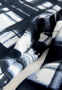 Textúrált szövet fekete, fehér és szürke absztrakt mintával, puha, hajlékony kialakítással és látható varrási részletekkel.