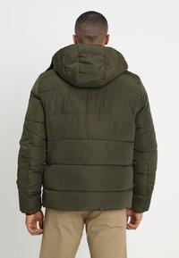 Oliven grøn polstret jakke med hætte, der har et horisontalt quiltet design, elastiske manchetter og en glat, skinnende overflade.