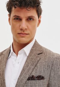 Szary w paski marynarka z białą koszulą. Posiada wzorzysty brązowy poszetkę. Gładka tekstura, dopasowany krój. Neutralne tło.