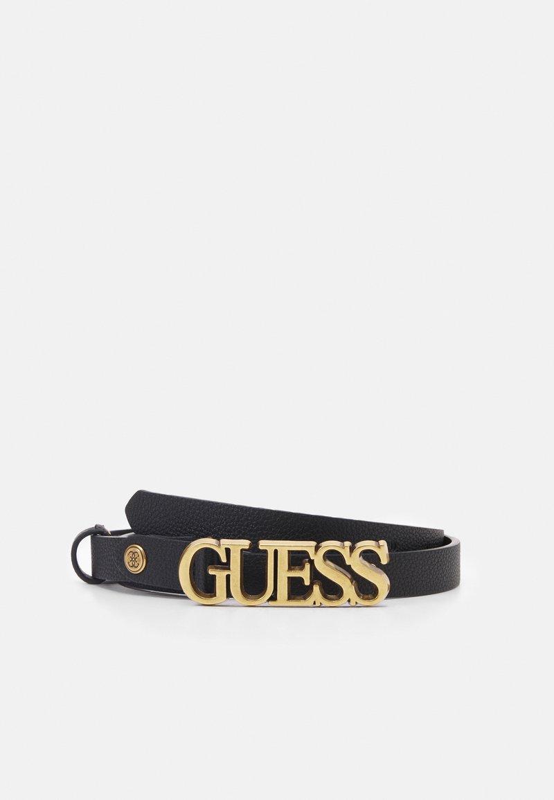 Ceinture en cuir noir avec une grande boucle dorée portant le logo GUESS et un petit emblème rond doré à l'extrémité de la lanière, présentée sur un fond blanc uni.