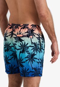 Maillots de bain pour hommes avec un dégradé de pêche à bleu et des imprimés de palmiers noirs. Comprend une taille élastique et une poche arrière.