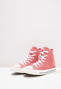 Czerwone płócienne sneakersy za kostkę z białymi sznurówkami, gumowym czubkiem i paskowanym spodem. Posiadają okrągłe logo po zewnętrznej stronie.