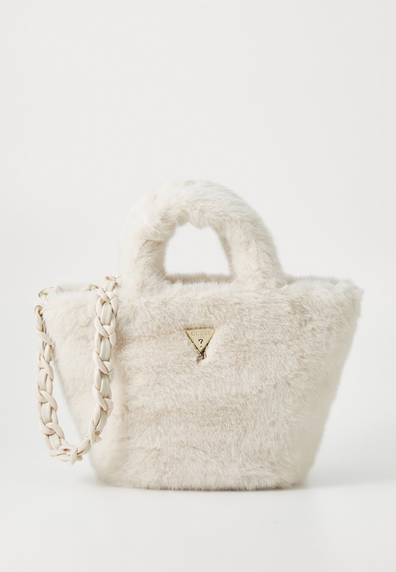 Sac en fausse fourrure de couleur blanc cassé avec un logo doré triangulaire, deux poignées courtes et une bandoulière tressée. Surface texturée.