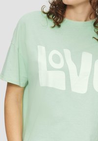Miętowa koszulka z krótkim rękawem z dużym białym napisem "Love" oraz lekko fakturowanym wykończeniem materiału.