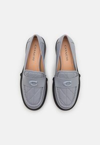 Mocassins en cuir matelassé gris avec une semelle en caoutchouc noire ; présentent un accent de logo circulaire sur un rabat. L'intérieur est doublé d'une matière beige lisse.
