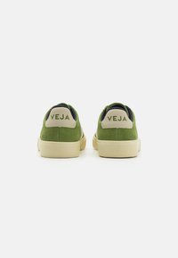 Grønne semskede sneakers med beige detaljer, som har en lav profil, flad sål og "VEJA" logo på hælen og siderne.