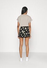 Světle hnědý top s krátkým rukávem v kombinaci s černou květinovou mini sukní s žlutými a bílými květy a bílými teniskami.