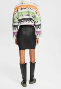 Gebreide trui met meerkleurige strepen en tekst, gecombineerd met een zwarte faux leren rok en zwart kniehoge laarzen met groene zolen.