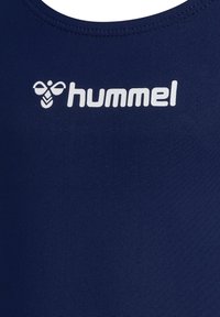 Débardeur de sport bleu marine avec une texture lisse, comportant un logo "hummel" blanc imprimé sur le devant. Aucun autre motif ou accent présent.