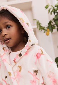 Puha polár fürdőköntös krémszínben, rózsaszín és arany balerina mintákkal. Kapucnival rendelkezik és átkötős, megkötős kialakítású.