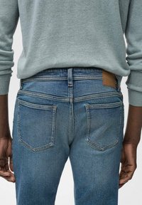 Vervaagde blauwe denim jeans gezien vanuit de achterkant, met twee achterzakken, een lichtbruine leren label op de tailleband en een getailleerd ontwerp.