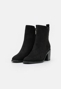 Botines de ante negros con punta redonda y tacón cuadrado. Presentan un cierre lateral y una textura suave con un diseño minimalista.