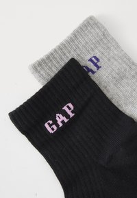 Chaussettes côtelées noires et grises avec des logos de marque contrastants ; la chaussette noire présente un texte rose, tandis que la chaussette grise arbore un texte violet.