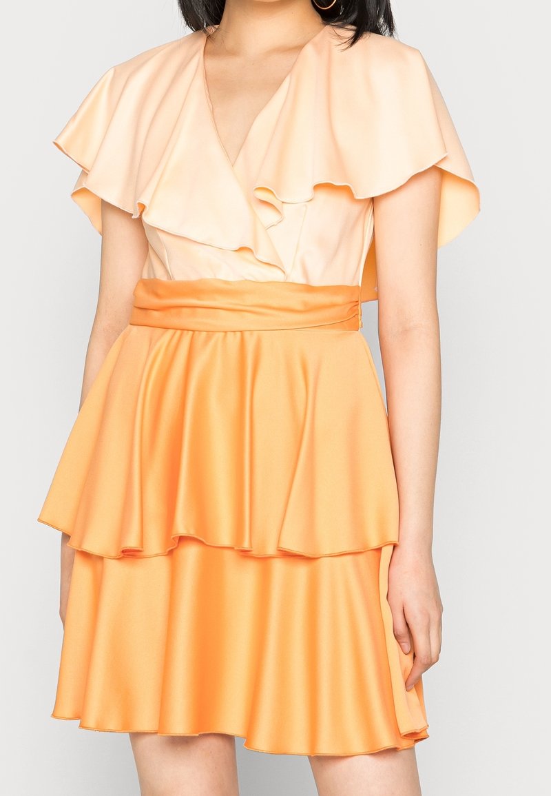 Robe courte orange avec volants superposés ; en tissu satin. Comprend un décolleté en V profond et une taille cintrée avec une ceinture assortie.