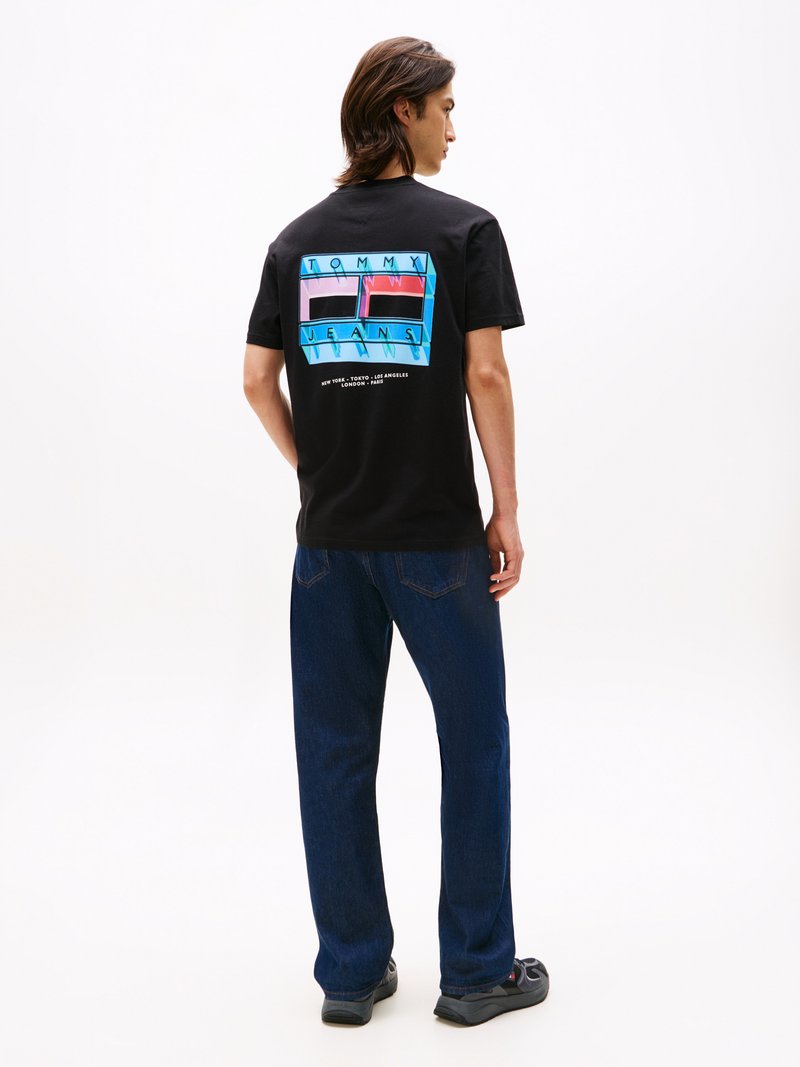 Melna kokvilnas T-kreklu ar krāsainu grafiku ar uzrakstu "TOMMY JEANS" aizmugurē. Apvienots ar zilām denima biksēm un tumšiem apaviem.
