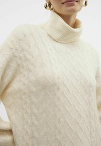 Kabelstickad polotröja i off-white, med diamant- och flätade mönster, mjuk textur och ribbad krage.