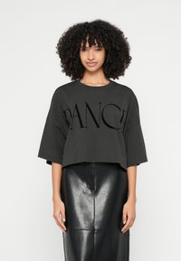 Zkrácené tmavě šedé tričko s výrazným černým nápisem „DANCE“ na přední straně. Má krátké rukávy a jednoduchý, uvolněný střih. Kombinováno s černou koženou sukní.