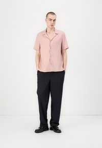 Camicia button-up rosa chiaro a maniche corte con colletto, abbinata a pantaloni pinstripati blu scuro e scarpe nere.