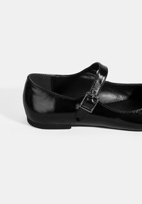 Schwarze Lackleder-Mary-Jane-Ballerina mit schmalem Riemen und Metallverschluss, featuring einer abgerundeten Spitze und niedrigem Absatz. Glatte Textur.