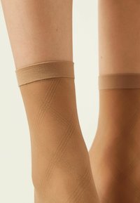 Beige ankelsokker lavet af gennemsigtigt materiale med et diagonalt rudemønster og en struktureret elastisk kant øverst.