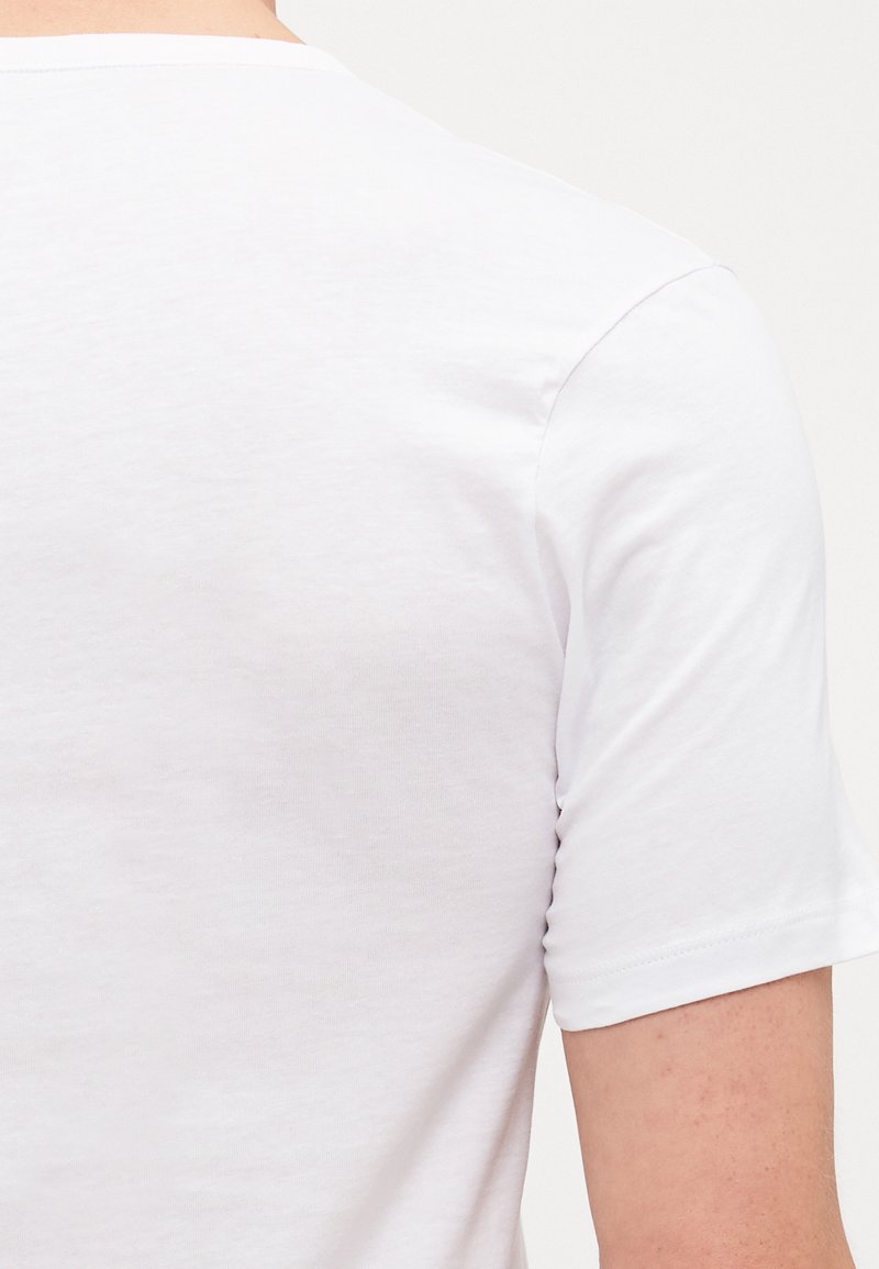 T-shirt en coton blanc avec des manches courtes, un col rond et une texture lisse, montrant le dos et la zone des épaules. Pas de motifs ni de designs visibles.