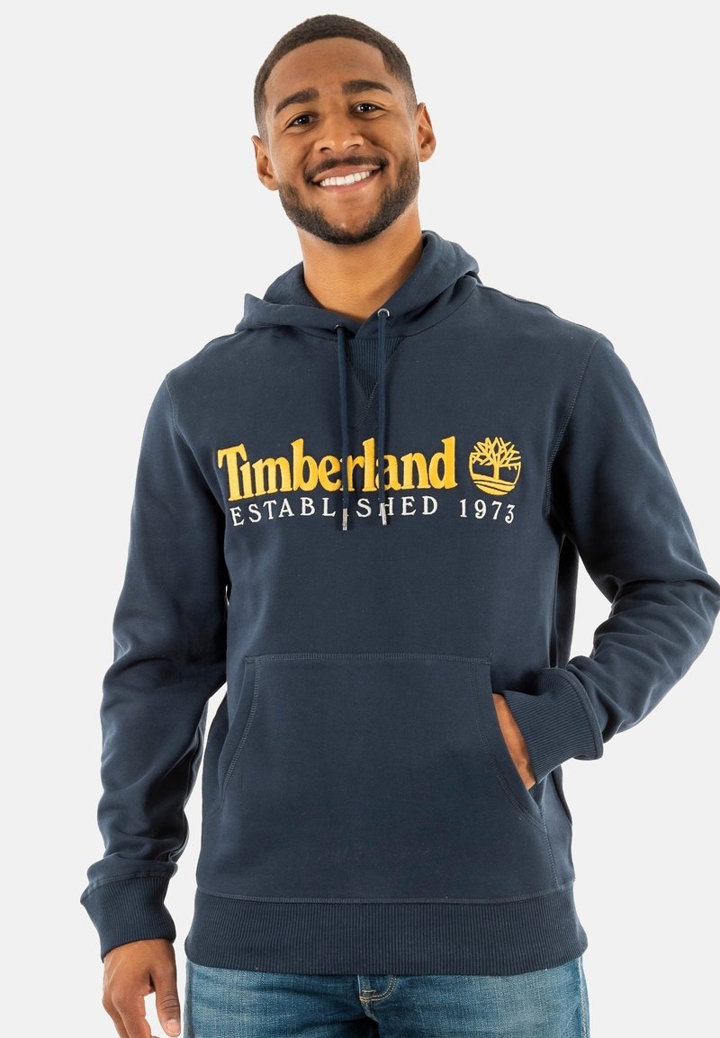 Navyblauwe katoenen hoodie met een voorkantzak, ribgebreide manchetten en een buidelzak. Het heeft gele Timberland-logo tekst en een boomgrafiek.