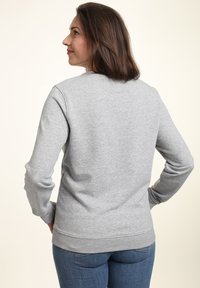 Felpa grigia con maniche lunghe, orlo e polsini a coste, texture morbida. Indossata sopra un paio di jeans blu, mostrata di spalle.